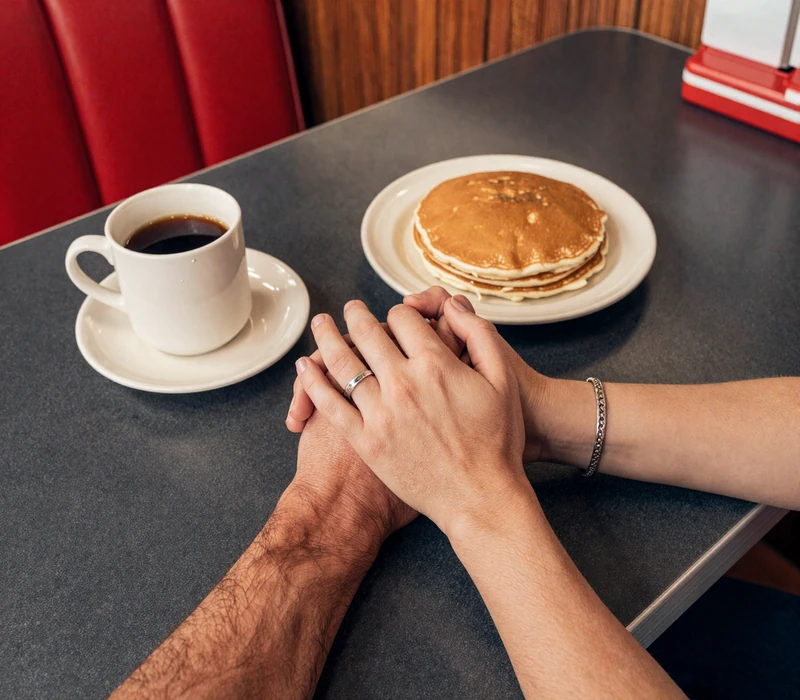 Trucker and partner clasping hands across a diner booth table, symbolizing the genuine connections RoadHeart's trucker dating service is built for